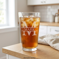 Illustrative mockup of a personalized pint glass with a large etched M and MARK across the center on a bright kitchen counter